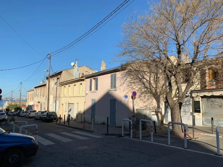 Rue pittoresque au village de la Madrague de Montredon à Marseille, avec bâtiments colorés et vue sur la mer.