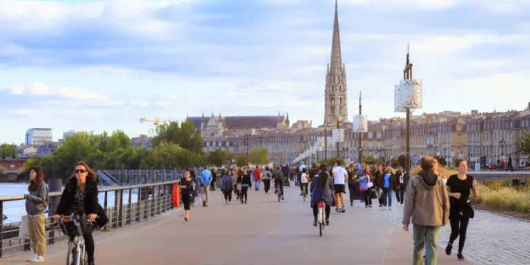 Promenade animée le long des quais de la Garonne à Bordeaux, avec vue sur l'architecture bordelaise et le clocher.