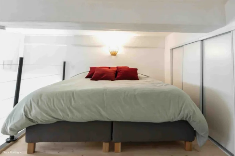 Chambre chaleureuse avec lit douillet et coussins rouges dans un appartement à Lyon