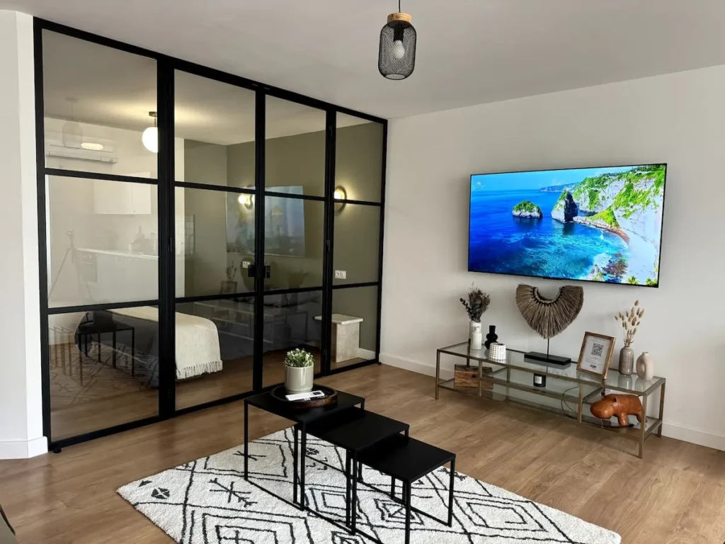 Intérieur moderne de l'appartement Casa Burdigala à Bordeaux, affichant un salon lumineux avec télévision et coin cuisine visible.