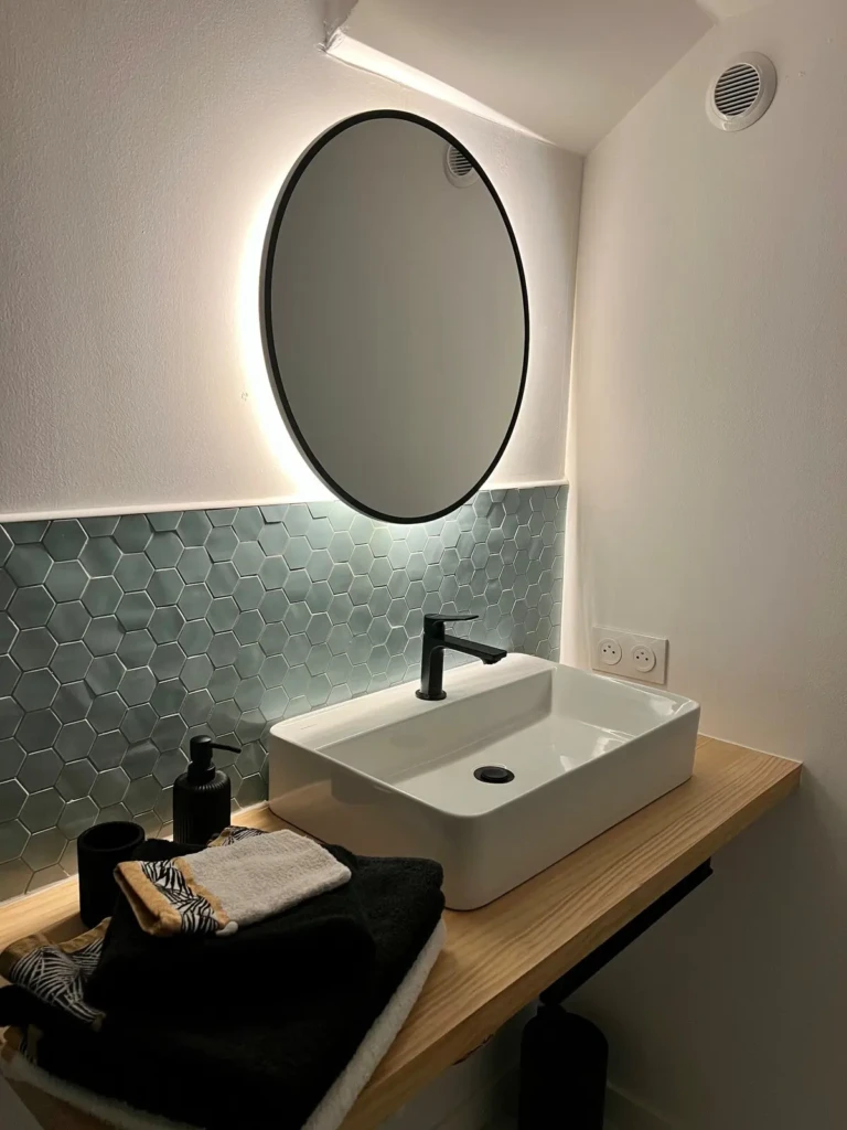 Salle de bain moderne avec lavabo design, miroir rond et serviettes confortables dans un studio à Bordeaux Saint Michel